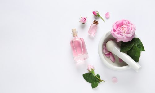 Composition with rose essential oil and flowers on white background, top view