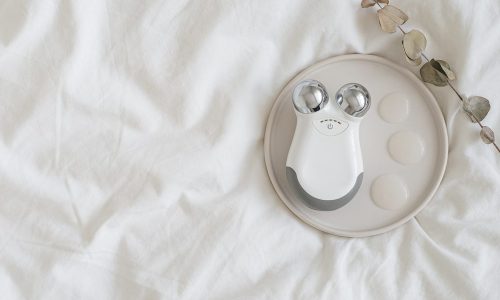 Microcurrent concept. Face massager with micro currents and gel primer drops. Home use device for anti-aging and face lifting on white bed. Top view or flat lay, copy space for text.